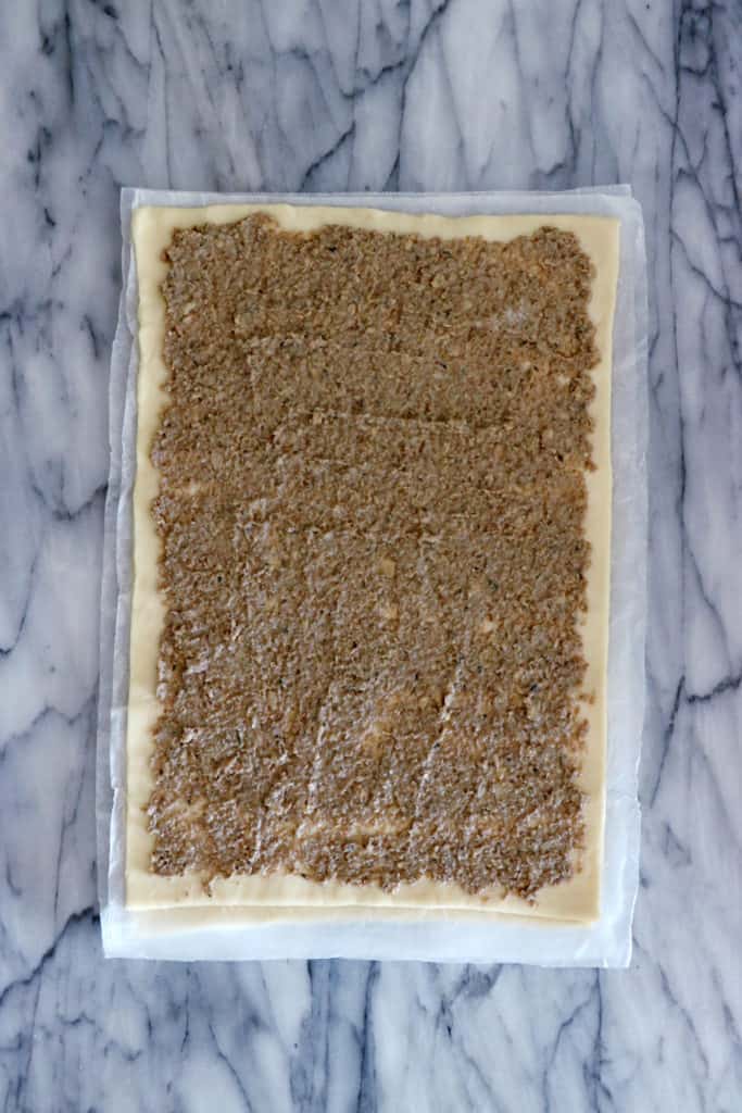 Spread savory topping on the first sheet of puff pastry.