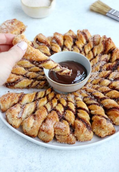 Vous ne résisterez pas à cette tarte soleil façon churros. Déchirez les torsades de pâte feuilletée recouvertes d'un mélange sucre-cannelle, trempez-les dans la sauce au chocolat chaud et dévorez sans plus attendre.