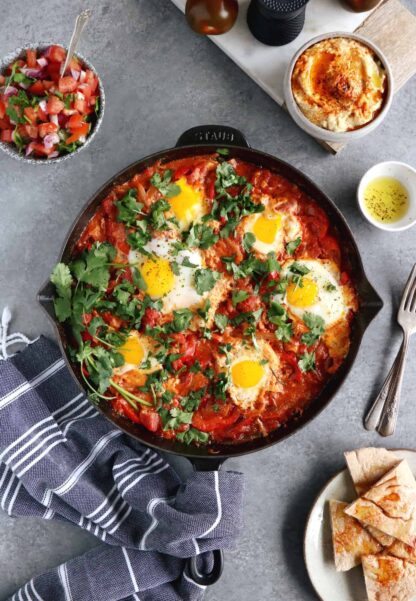 Shakshuka with Feta Cheese is a simple dish consisting of poached eggs in a simmering tomato sauce with feta and spices, traditionally served in a cast iron skillet.